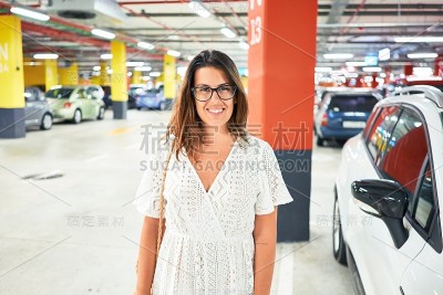 年轻女子自信地微笑在地下停车场周围的汽车和灯光