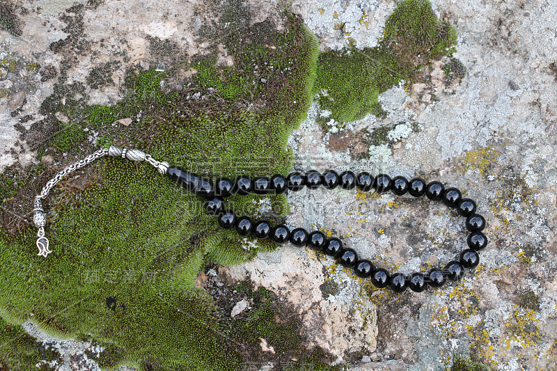 A black prayer beads on mossy rocks.