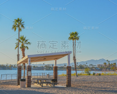美国亚利桑那州莫哈维县哈瓦苏湖扶轮社区公园的遮荫树冠及棕榈树下的烧烤及野餐桌