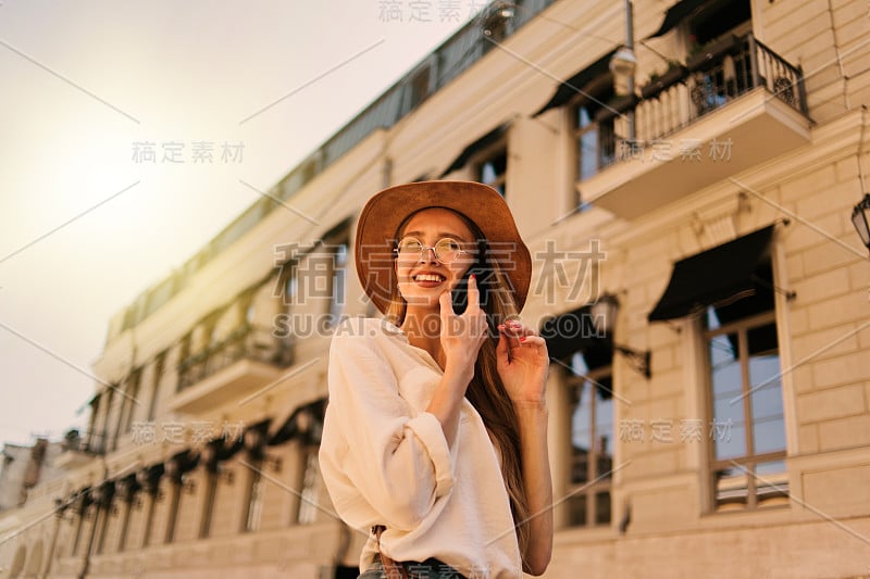 年轻随意风格的女人在毡帽谈论电话对城市建筑的背景