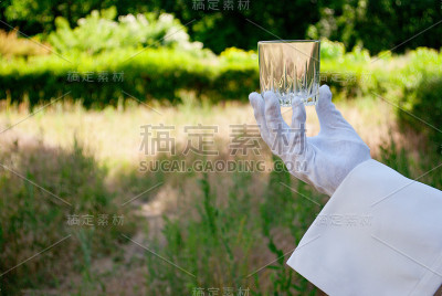 在大自然中，一个戴着白手套的服务员的手拿着一个玻璃杯