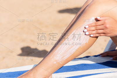 在海边的日光浴床上，一个漂亮的女人正在用手往腿上涂防晒霜