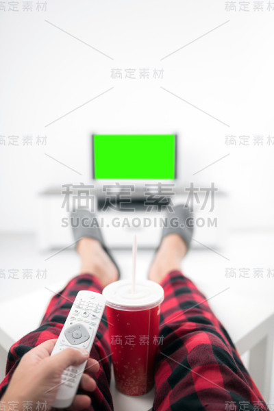 在客厅的桌子上，男人一边喝着汽水，一边看电视。色度键绿色屏幕。
