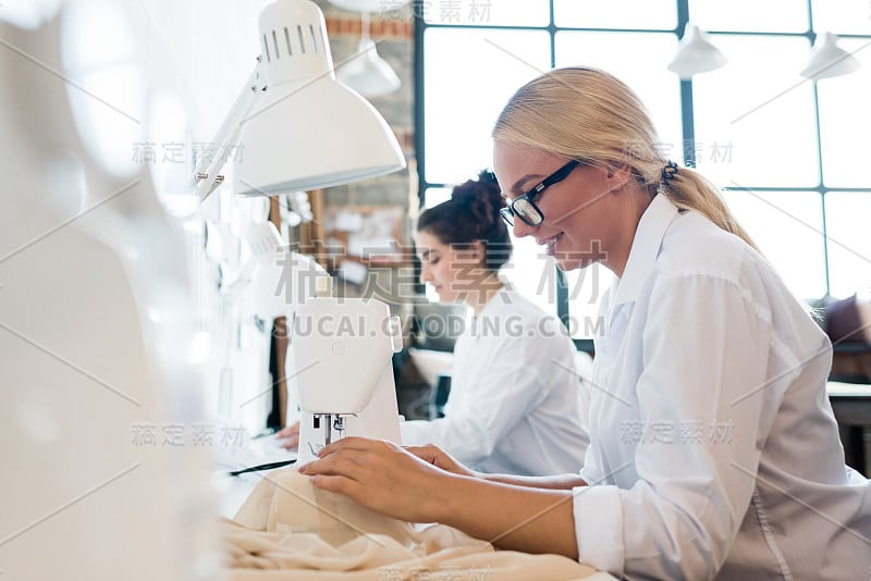 女裁缝穿着白衬衫缝制衣服或亚麻布的年轻漂亮的女裁缝