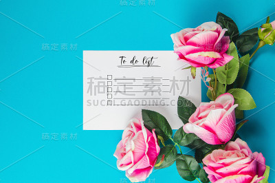 粉色玫瑰与一张纸与待做清单上的蓝色背景