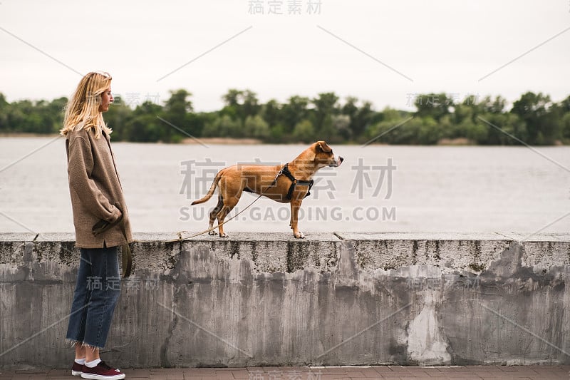 阴天里，一个女人和她的狗站在河边