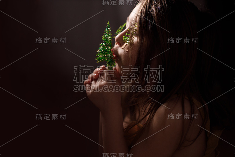 生态学的概念，小女孩的肖像与蕨类植物的小枝贴在她的脸颊上，拿着小枝