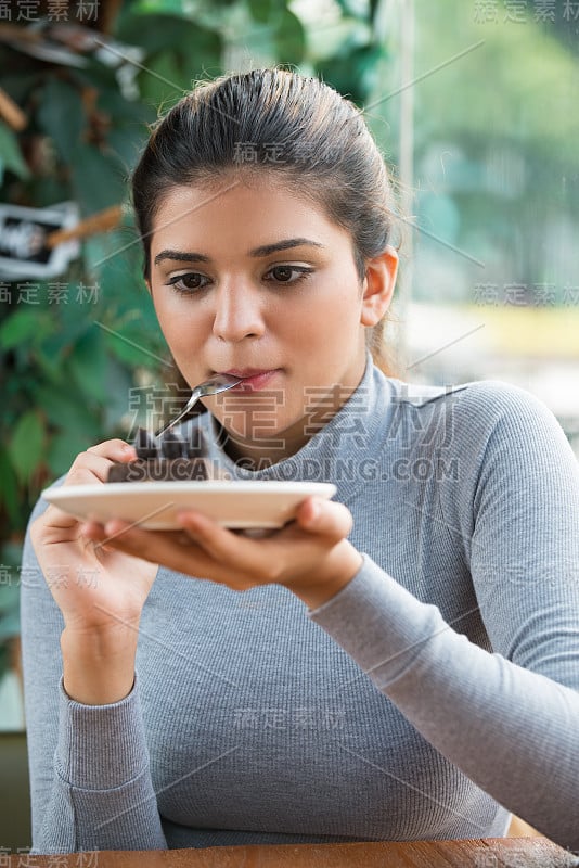 快乐的年轻女子在咖啡馆吃盘子里的蛋糕