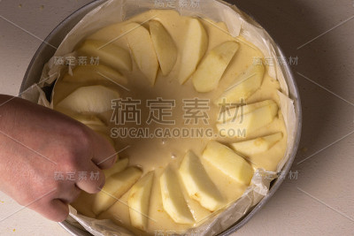 烘烤前，女性将苹果片放在蛋糕上。