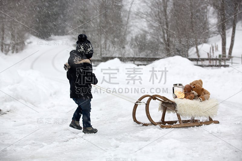 可爱的男孩在雪地里玩泰迪熊，冬天的时候。小孩子在下雪天玩玩具