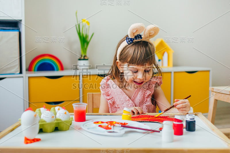 蹒跚学步的小女孩用纸母鸡画兔子耳朵作为复活节装饰