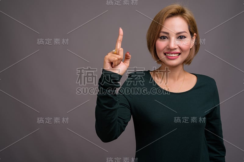 工作室拍摄的美丽的亚洲女人短发穿着长袖绿色连衣裙，以灰色的背景