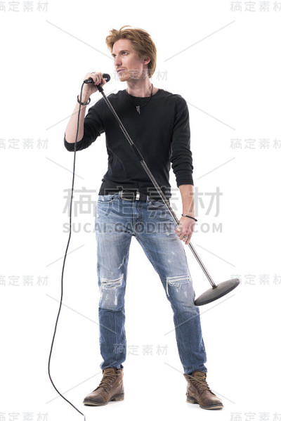 英俊的歌手在牛仔裤拿着麦克风摆姿势和看别处。