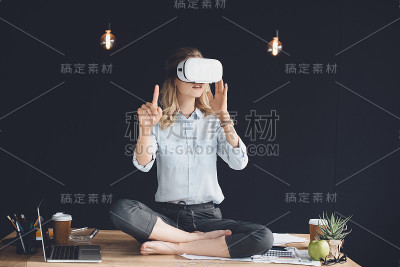 女商人在虚拟现实耳机坐在莲花姿势在桌子上的办公室