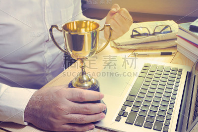 商人拿着奖杯，感觉像一个胜利者在他的工作桌上，金融概念。