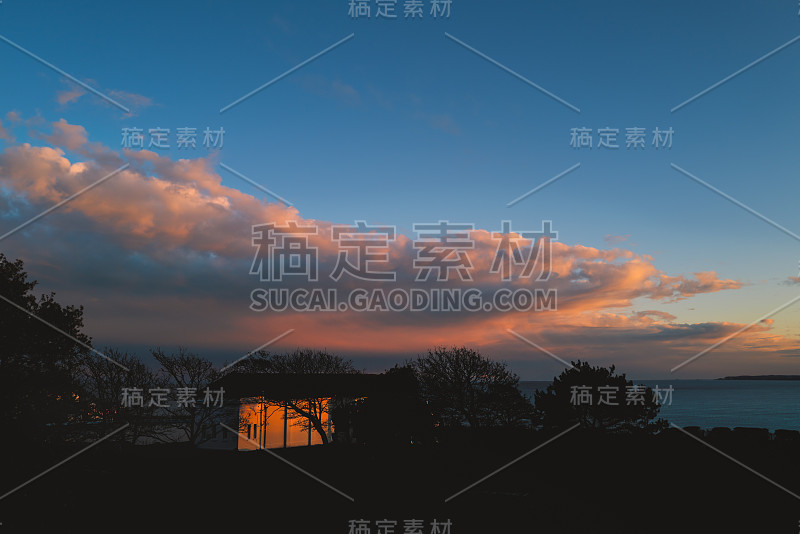 在一个明亮的冬天的晚上，夕阳反射在划船游泳池建筑的背面和剪影的一棵树。