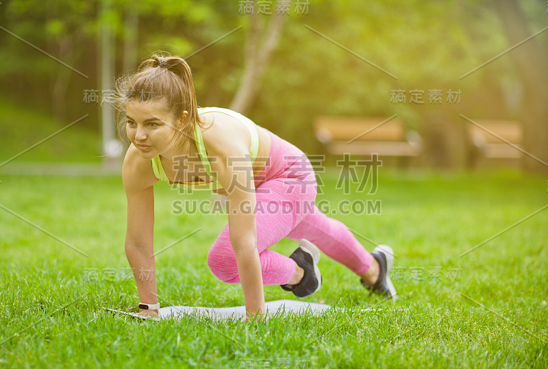 运动健康的妇女做有氧运动在一个垫子上的公园户外