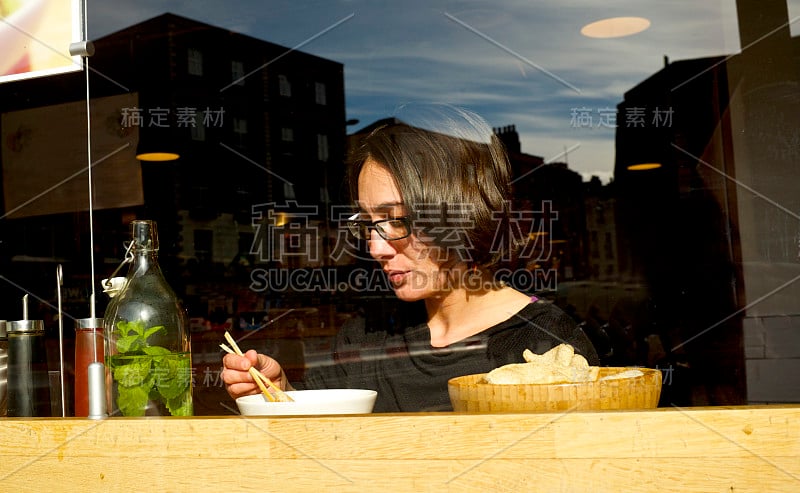 女孩在餐厅前窗边吃亚洲面条，反应灵敏