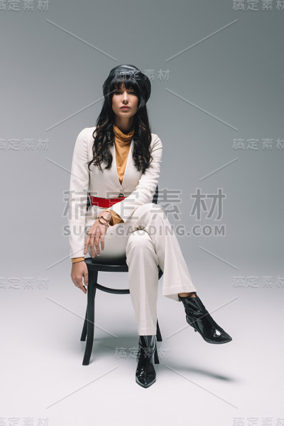 漂亮的黑发女人穿着白色的套装坐在灰色的椅子上