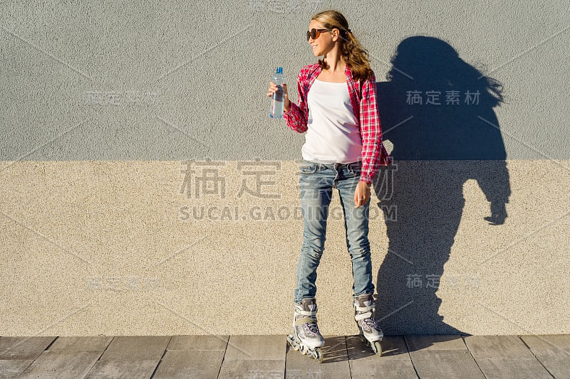 年轻女孩拿着一瓶水，穿着滚轴鞋。背景灰墙，拷贝空间