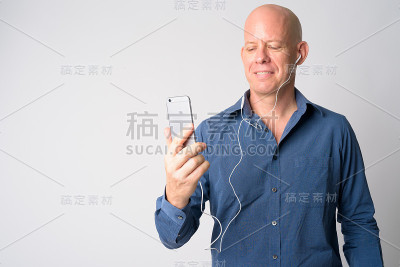 快乐成熟的秃头商人肖像使用电话和听音乐
