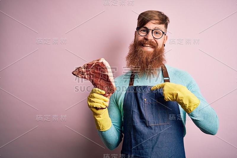 红头发的爱尔兰屠夫与胡子拿生牛肉在粉红色的背景与惊讶的脸指向自己的手指