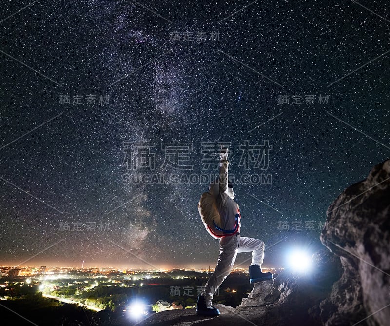 太空旅行者站在布满星星的夜空下的岩石山上。