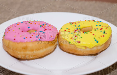 白色盘子上浇了一层酱汁的甜甜圈。彩色甜面包圈