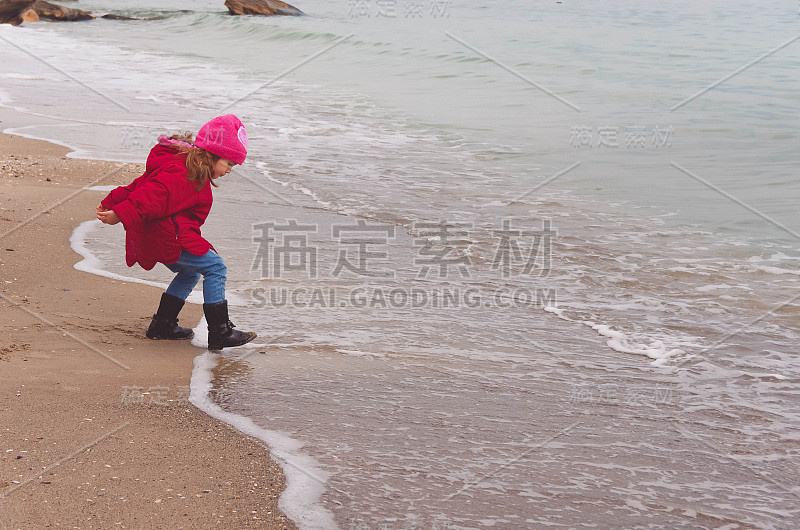 穿着红夹克的小女孩在海滩上玩海浪