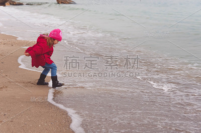 穿着红夹克的小女孩在海滩上玩海浪