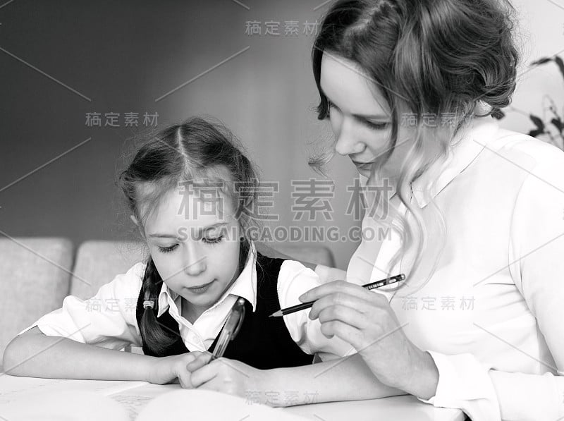 妈妈在家里帮助女儿做作业。黑色和白色。