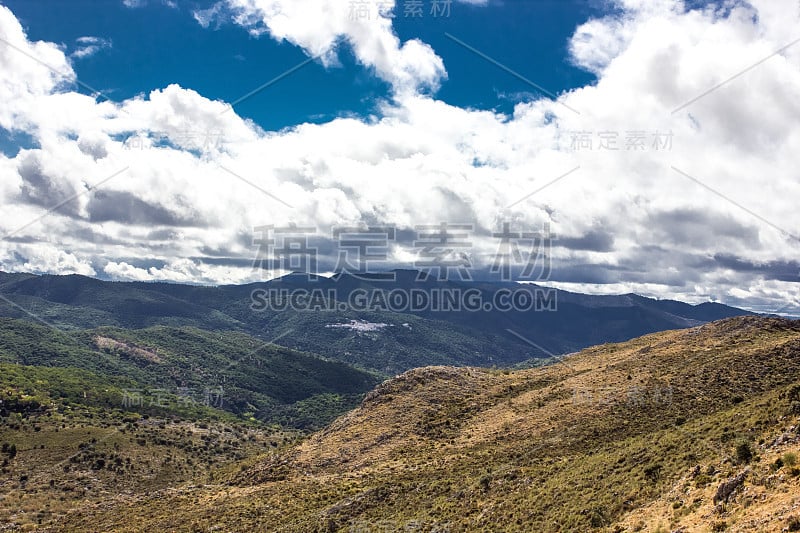 山景上的蓝色多云的天空背景。风景如画的群山在阳光下闪闪发光。令人屏息的自然影像