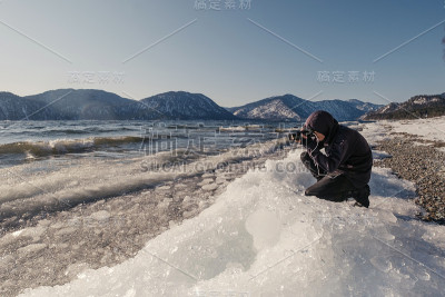 摄影师在阳光明媚的日子里拍摄山上的冬季冰湖