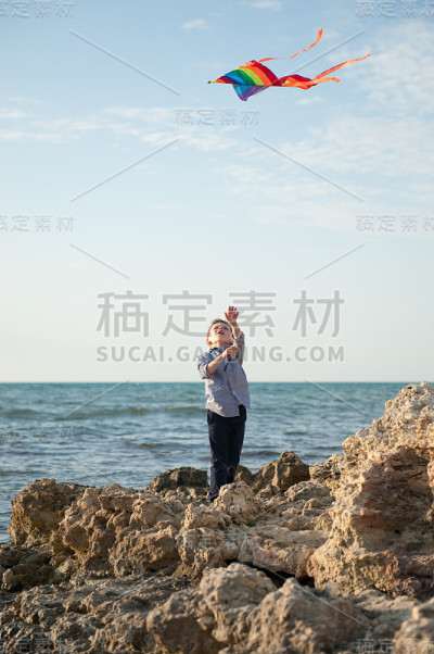 一个小男孩拿着风筝站在岩石上靠海