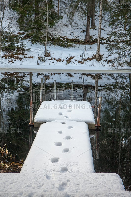 瑞典的冬季景观。湖面上正在融化的雪。雪地上有男人的痕迹，码头上有。