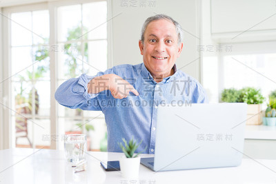 英俊的高级男子使用电脑笔记本电脑在网上工作与惊讶的脸指向自己