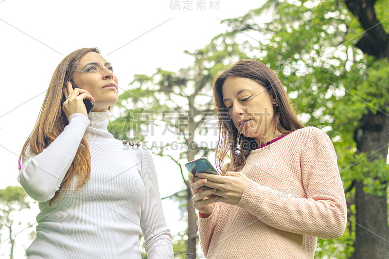 一个年轻女子在讲手机，她的朋友在看她的智能手机。