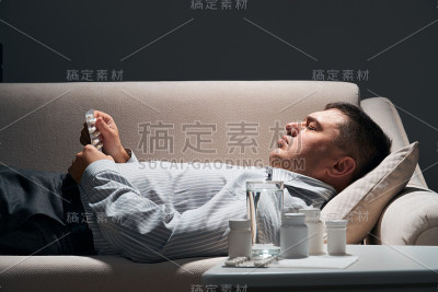 劳累过度的商人正躺在沙发上休息。药片和一杯水就在他身边。