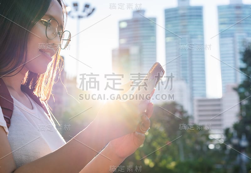 不同的亚洲潮女使用手机在城市公园与明亮的阳光在下午