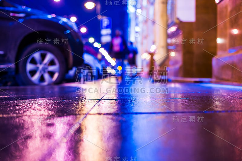 秋雨夜城。大街上有很多人。停着的汽车。商店橱窗里的灯光反射在人行道上。