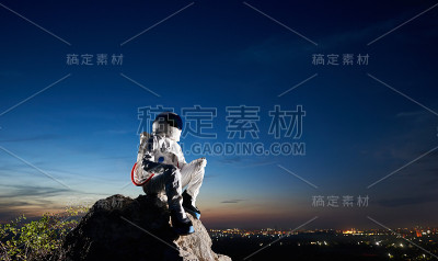 太空旅行者坐在岩石山在蓝天下。