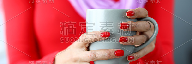 女性的手与红色指甲拿着灰色的咖啡杯