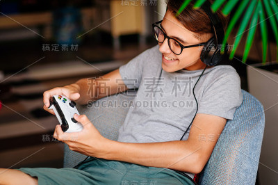 微笑的少年坐在室内的椅子上戴着耳机玩游戏机
