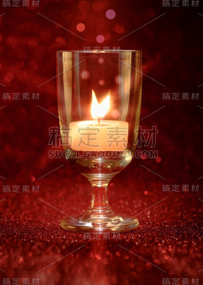金色的烛光在酒杯中燃烧，带有灯光效果和红色模糊的散景背景