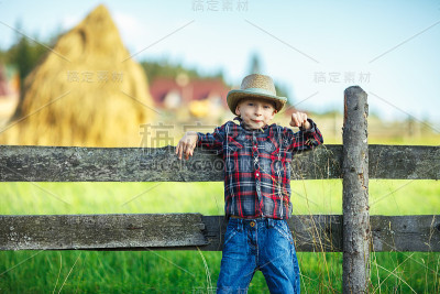 小男孩的背景是模糊的大草堆和村庄景观
