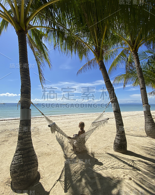 天堂度假村，女孩侧身坐在吊床上。美丽的海滩、棕榈树、海洋