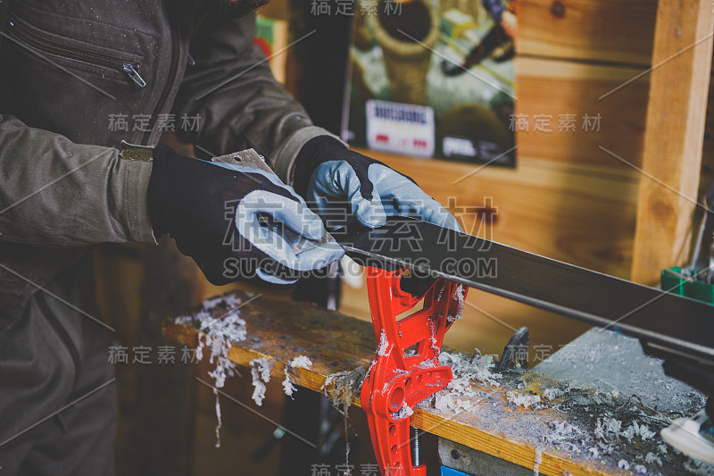 滑雪板维修车间的一名男工人正在修理滑雪板的滑动表面。特写的手与塑料刮除蜡，去除新的蜡。主题修复的滑雪