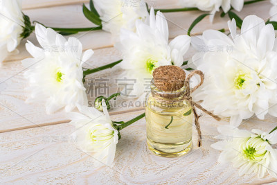 菊花精油装在玻璃瓶旁边的白色菊花表面上。水疗、美容、护肤、美容的概念。
