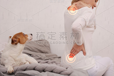 背痛的女人坐在家里的床上。缓解疼痛的概念。