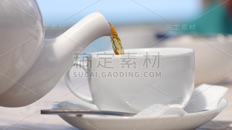 在海边的海滩咖啡馆里，白色茶壶把茶倒进杯子里